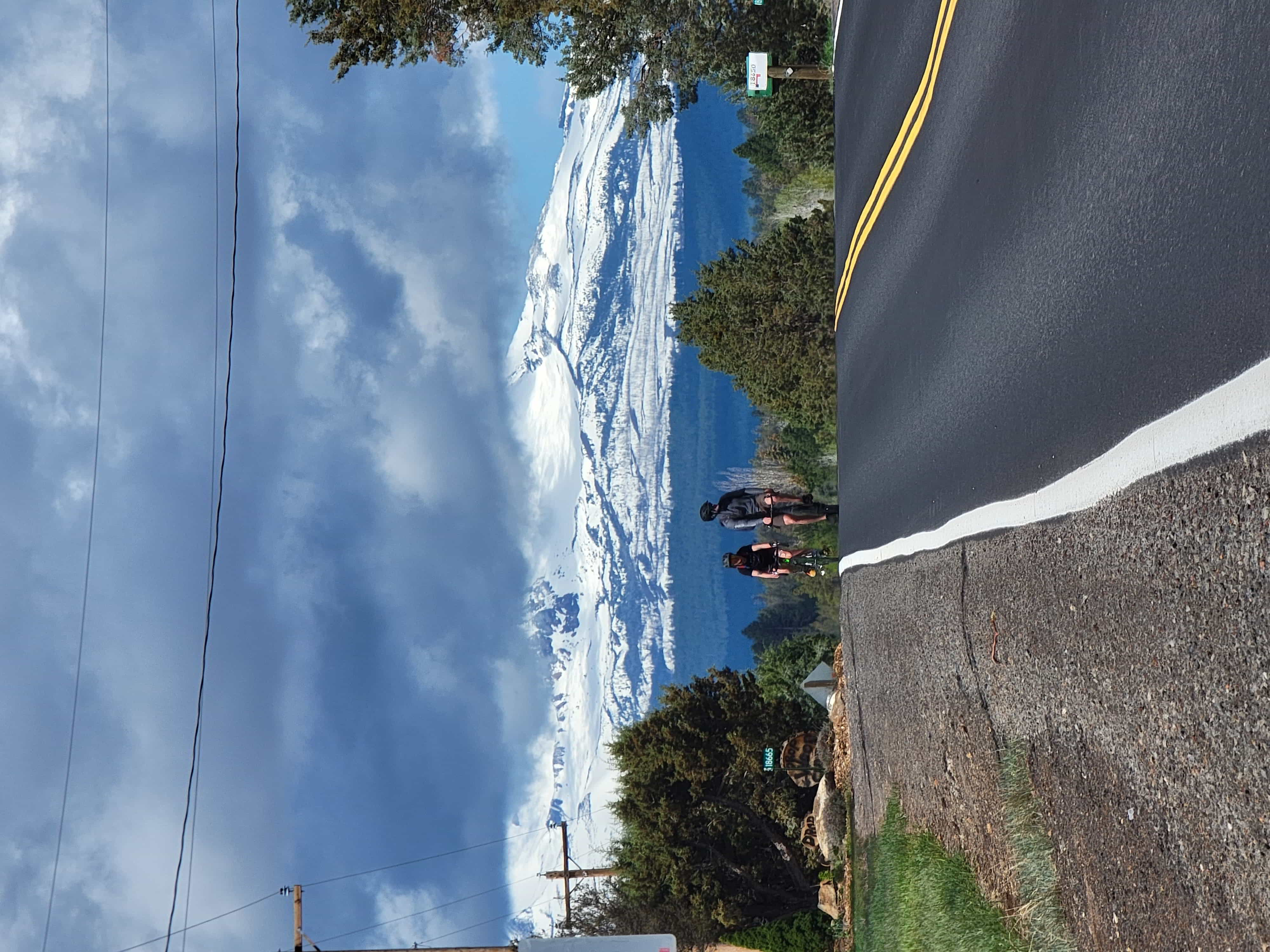 2 people biking towards the camera on a two lane backroad, with south sister mountain in the background